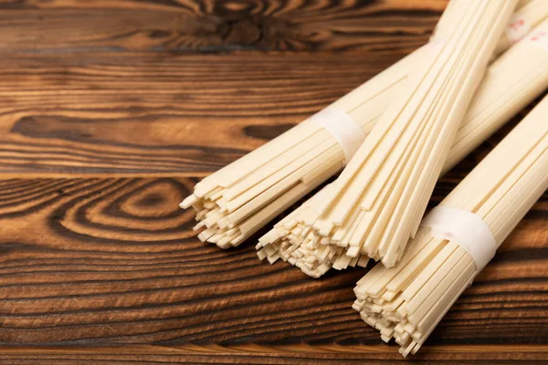 stock image Rice noodles on a brown textured wooden background. Raw funchose noodles and rice groats. Thai dried rice noodles. Place for text. Place to copy. Close-up.