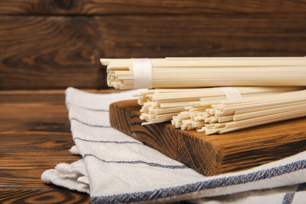 Рисовая лапша на коричневом деревянном фоне. Сырая лапша и рисовая крупа. Тайская сушеная рисовая лапша. Место для смс. Место для копирования. Крупный план.