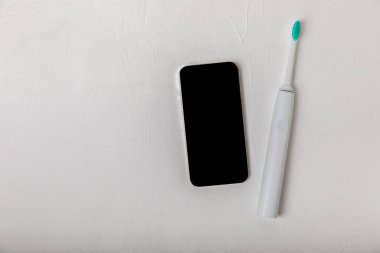Beyaz mermer arka plandaki akıllı telefon uygulamasına kablosuz bağlantısı olan sonik elektrikli diş fırçası. Modern ev teknolojisi konsepti. Ağız ve sakız bakımı. Tıp konsepti. Dişçi.