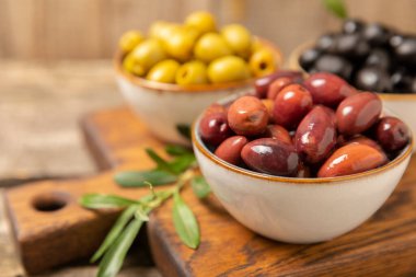Eski ahşap bir arka planda yeşil, siyah ve kırmızı zeytinlerin yaprakları var. Lezzetli ve sağlıklı yiyecekler. Lezzetli. Akdeniz mutfağı. Mesaj için yer. kopyalama alanı.
