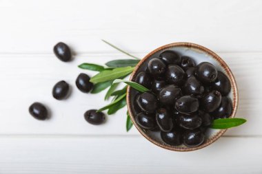 Beyaz ahşap kaplamalı yapraklı bir kasede siyah zeytin. Lezzetli ve sağlıklı yiyecekler. Hassasiyet. Salata ve kokteyl malzemesi. Akdeniz mutfağı. Yakın plan. Mesaj için yer. kopyalama alanı.