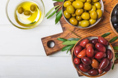 Beyaz arka planda yeşil, kırmızı ve siyah zeytin seti. Taze zeytin yapraklı zeytin yağı ve kâse içinde çeşitli zeytin türleri. Lezzetli. Akdeniz mutfağı. Boşluğu kopyala.