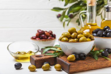Beyaz arka planda yeşil, kırmızı ve siyah zeytin seti. Taze zeytin yapraklı zeytin yağı ve kâse içinde çeşitli zeytin türleri. Lezzetli. Akdeniz mutfağı. Boşluğu kopyala.