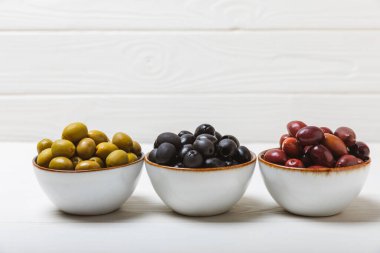 Beyaz arka planda yeşil, kırmızı ve siyah zeytin seti. Taze zeytin yapraklı zeytin yağı ve kâse içinde çeşitli zeytin türleri. Lezzetli. Akdeniz mutfağı. Boşluğu kopyala.