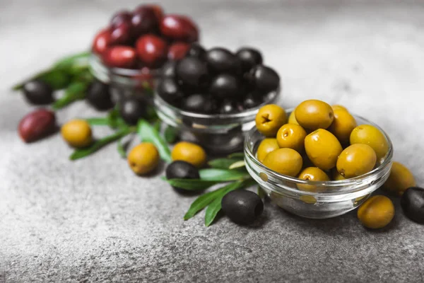 stock image A set of green, red and black olives on a black marble background. Different types of olives in bowls and olive oil with fresh olive leaves. Delicacy.Mediterranean Kitchen. Copy space.