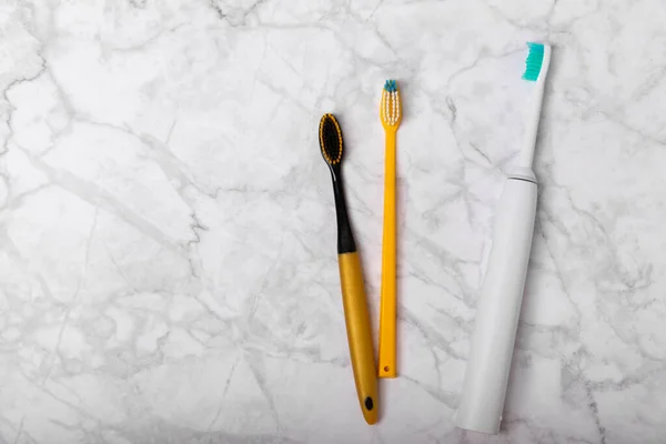 Electric and manual toothbrushes on a marble background. View from above. Oral hygiene. Ordinary toothbrush, eco and electric toothbrush. Oral hygiene. Oral Care Kit. Dentist concept. Dental care