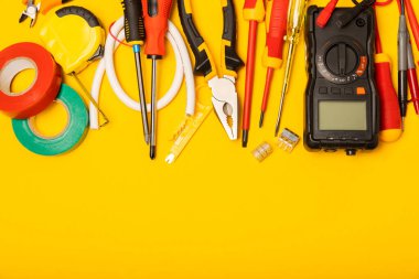 Sarı zemin üzerindeki elektrik teçhizatı kopya alanı ile üst görünüm. Elektrik aracı seti. Çoklu metre, testçi, tornavida, kesiciler, koli bandı, lamba, mezura, mezura ve kablo..