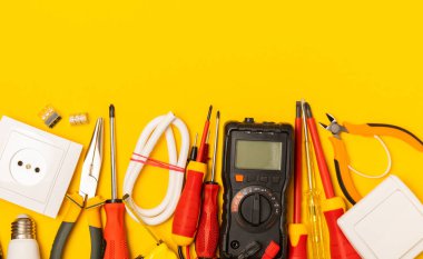 Sarı zemin üzerindeki elektrik teçhizatı kopya alanı ile üst görünüm. Elektrik aracı seti. Çoklu metre, testçi, tornavida, kesiciler, koli bandı, lamba, mezura, mezura ve kablo..