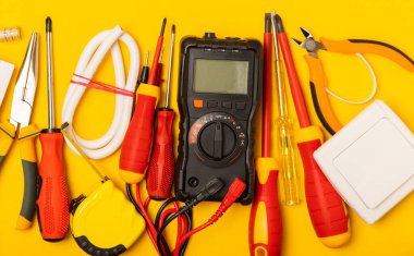 Sarı zemin üzerindeki elektrik teçhizatı kopya alanı ile üst görünüm. Elektrik aracı seti. Çoklu metre, testçi, tornavida, kesiciler, koli bandı, lamba, mezura, mezura ve kablo..