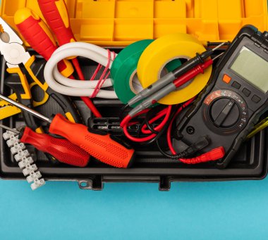 Mavi arka planda kopyalanmış elektrik teçhizatı. Üst görünüm. Elektrik aracı seti. Çoklu metre, test cihazı, tornavida, kesici, koli bandı, lamba, mezura, mezura ve kablo..