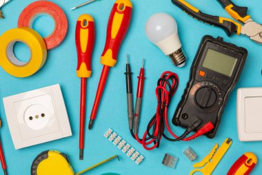 Mavi arka planda kopyalanmış elektrik teçhizatı. Üst görünüm. Elektrik aracı seti. Çoklu metre, test cihazı, tornavida, kesici, koli bandı, lamba, mezura, mezura ve kablo..