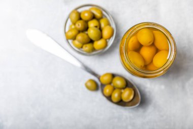 Beton bir arka planda cam kavanozda zeytinler. Kavanozda yeşil zeytin. Cam kavanozda turşulu zeytin. Ahşap bir arka planda. Salamura zeytin. Mesaj için yer var. Kopya için yer var. Vejetaryen yemeği.