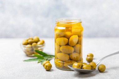 Beton bir arka planda cam kavanozda zeytinler. Kavanozda yeşil zeytin. Cam kavanozda turşulu zeytin. Ahşap bir arka planda. Salamura zeytin. Mesaj için yer var. Kopya için yer var. Vejetaryen yemeği.