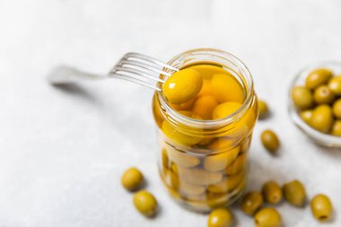 Mutfak masasındaki çatallı ve cam kavanozlu zeytinlere yakın çekim. Kavanozda yeşil zeytin. Cam kavanozda turşulu zeytin. Ahşap bir arka planda. Salamura zeytin. Mesaj için yer var. Kopya için yer var. Vejetaryen yemeği.