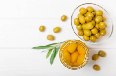 Beyaz ahşap arka planda cam bir kavanozda zeytin. Kavanozda yeşil zeytin. Cam kavanozda turşulu zeytin. Ahşap bir arka planda. Salamura zeytin. Mesaj için yer var. Kopya için yer var. Vejetaryen yemeği.