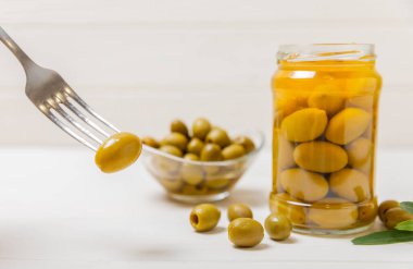 Mutfak masasındaki çatallı ve cam kavanozlu zeytinlere yakın çekim. Kavanozda yeşil zeytin. Cam kavanozda turşulu zeytin. Ahşap bir arka planda. Salamura zeytin. Mesaj için yer var. Kopya için yer var. Vejetaryen yemeği.