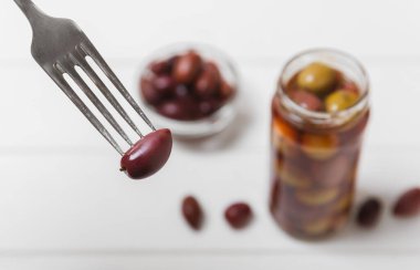 Mutfak masasındaki çatallı ve cam kavanozlu zeytinlere yakın çekim. Kavanozda yeşil zeytin. Cam kavanozda turşulu zeytin. Ahşap bir arka planda. Salamura zeytin. Mesaj için yer var. Kopya için yer var. Vejetaryen yemeği.