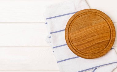 Mutfak masasının üzerinde boş ahşap yuvarlak pizza tahtası. Kırmızı kareli mutfak havlusuyla kesme tahtası. Tahta pizza tabağı, kopyalama alanı. Mutfak eşyaları. Yemek tarifi. Mesaj için yer. Düz yatıyordu.
