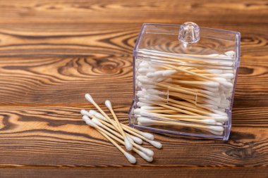 Kahverengi ahşap arka planda beyaz pamuklu çubuklar. Pamuk tomurcukları. Bambu pamuk tomurcukları. Çevre dostu. Kulaklar için hijyenik pamuklu bez. Mesaj için yer. Kopyalanacak yer.