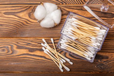 Kahverengi ahşap arka planda beyaz pamuklu çubuklar. Pamuk tomurcukları. Bambu pamuk tomurcukları. Çevre dostu. Kulaklar için hijyenik pamuklu bez. Mesaj için yer. Kopyalanacak yer.