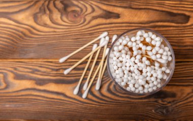 Kahverengi ahşap arka planda beyaz pamuklu çubuklar. Pamuk tomurcukları. Bambu pamuk tomurcukları. Çevre dostu. Kulaklar için hijyenik pamuklu bez. Mesaj için yer. Kopyalanacak yer.