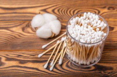 Kahverengi ahşap arka planda beyaz pamuklu çubuklar. Pamuk tomurcukları. Bambu pamuk tomurcukları. Çevre dostu. Kulaklar için hijyenik pamuklu bez. Mesaj için yer. Kopyalanacak yer.