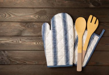 Mutfak eşyaları. Kahverengi ahşap arka planda sıcak yemekler için fırın eldiveni ve tencere tutacağı. Yakın plan. Mesaj için yer. Boşluğu kopyala.