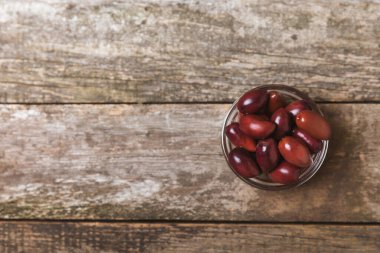 Kahverengi ahşap arka planda kırmızı zeytin. Taze zeytin yapraklı zeytin yağı ve kâse içinde çeşitli zeytin türleri. Uzayı kopyala Mesaj için yer. Akdeniz yemekleri. Vejetaryen.