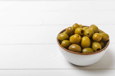 Beyaz ahşap arka planda yeşil zeytin. Taze zeytin yapraklı zeytin yağı ve kâse içinde çeşitli zeytin türleri. Uzayı kopyala Mesaj için yer. Akdeniz yemekleri. Vejetaryen.