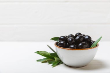 Beyaz ahşap arka planda siyah zeytin. Taze zeytin yapraklı zeytin yağı ve kâse içinde çeşitli zeytin türleri. Uzayı kopyala Mesaj için yer. Akdeniz yemekleri. Vejetaryen.