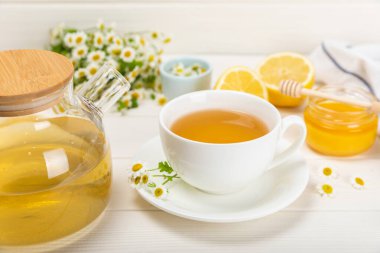 Kahverengi desenli beyaz bir fincanda papatya çayı. Papatya çiçekleriyle dolu doğal bir saat. Bitki çayı. Dokunulmazlık çayı. Doğal iyileştirici kavramı. Sağlıklı detoks içeceği. Kapatın. Mesaj için yer. Boşluğu kopyala.