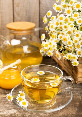 Kahverengi desenli arka planda cam bir fincanda papatya çayı. Papatya çiçekleriyle dolu doğal bir saat. Bitki çayı. Dokunulmazlık çayı. Doğal iyileştirici kavramı. Sağlıklı detoks içeceği. Kapatın. Metin için yer.