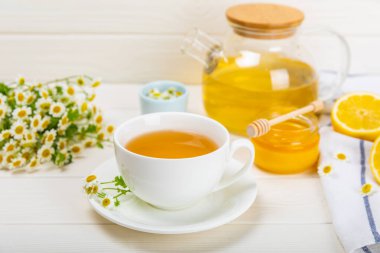 Beyaz tahta bir masada, bal, limon ve papatya buketiyle beyaz bir fincanda bitkisel papatya çayı. Yakın plan. Uzayı kopyala Faydalı bitkisel içecekler, bağışıklık çayı. Doğal şifacı kavramı.