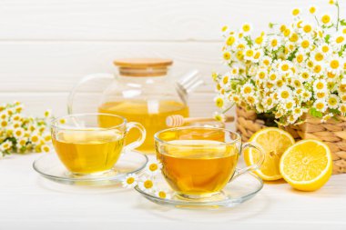 Beyaz ahşap bir masada, bal, limon ve papatya çiçekli cam bir fincanda papatya çayı. Yakın plan. Uzayı kopyala Faydalı bitkisel içecekler, bağışıklık çayı. Doğal şifacı kavramı. Metin için yer..