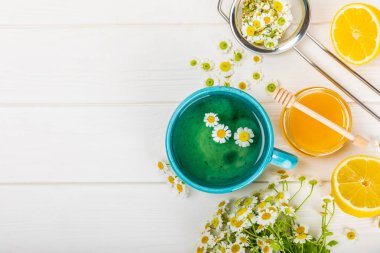Beyaz ahşap bir masada, bal, limon ve papatya buketi ile mavi bir fincanda papatya çayı. Yakın plan. Uzayı kopyala Faydalı bitkisel içecekler, bağışıklık çayı. Doğal şifacı kavramı. Metin için yer..