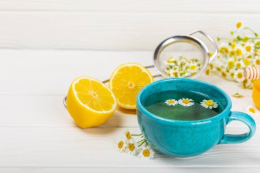 Beyaz ahşap bir masada, bal, limon ve papatya buketi ile mavi bir fincanda papatya çayı. Yakın plan. Uzayı kopyala Faydalı bitkisel içecekler, bağışıklık çayı. Doğal şifacı kavramı. Metin için yer..