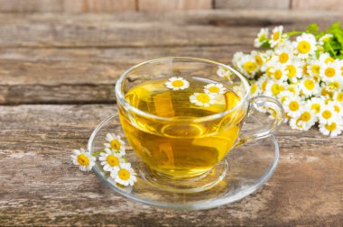 Kahverengi ahşap bir masada, içinde bal, limon ve papatya buketi olan cam bir fincanda papatya çayı. Yakın plan. Uzayı kopyala sağlıklı bitkisel içecekler, bağışıklık çayı. Doğal şifacı kavramı. Metin için yer..