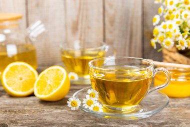 Kahverengi ahşap bir masada, içinde bal, limon ve papatya buketi olan cam bir fincanda papatya çayı. Yakın plan. Uzayı kopyala sağlıklı bitkisel içecekler, bağışıklık çayı. Doğal şifacı kavramı. Metin için yer..