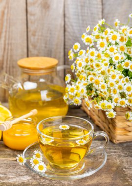 Kahverengi ahşap bir masada, içinde bal, limon ve papatya buketi olan cam bir fincanda papatya çayı. Yakın plan. Uzayı kopyala sağlıklı bitkisel içecekler, bağışıklık çayı. Doğal şifacı kavramı. Metin için yer..