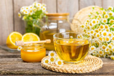 Kahverengi ahşap bir masada, içinde bal, limon ve papatya buketi olan cam bir fincanda papatya çayı. Yakın plan. Uzayı kopyala sağlıklı bitkisel içecekler, bağışıklık çayı. Doğal şifacı kavramı. Metin için yer..