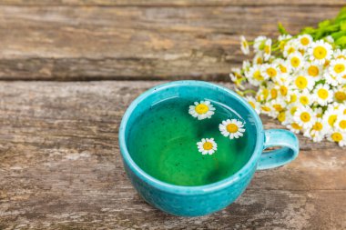 Kahverengi ahşap bir masada, içinde bal, limon ve papatya buketi olan mavi bir fincanda papatya çayı. Yakın plan. Uzayı kopyala sağlıklı bitkisel içecekler, bağışıklık çayı. Doğal şifacı kavramı. Metin için yer..