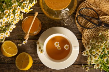 Kahverengi ahşap bir masada, bal, limon ve papatya buketli bir fincan papatya çayı. Yakın plan. Uzayı kopyala sağlıklı bitkisel içecekler, bağışıklık çayı. Doğal şifacı kavramı. Metin için yer..