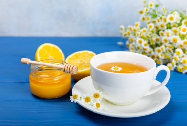 Mavi ahşap bir masada, bal, limon ve papatya çiçekli bir fincanda papatya çayı. Yakın plan. Uzayı kopyala sağlıklı bitkisel içecekler, bağışıklık çayı. Doğal şifacı kavramı. Metin için yer..