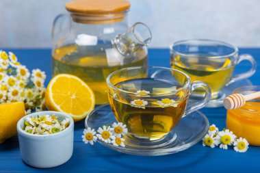 Mavi ahşap bir masada, bal, limon ve papatya çiçekli bir fincanda papatya çayı. Yakın plan. Uzayı kopyala sağlıklı bitkisel içecekler, bağışıklık çayı. Doğal şifacı kavramı. Metin için yer..