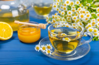 Mavi ahşap bir masada, bal, limon ve papatya çiçekli bir fincanda papatya çayı. Yakın plan. Uzayı kopyala sağlıklı bitkisel içecekler, bağışıklık çayı. Doğal şifacı kavramı. Metin için yer..