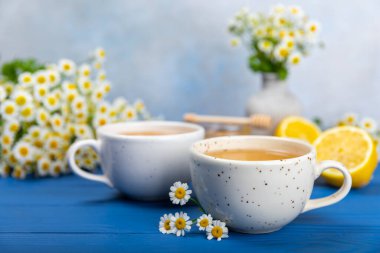 Mavi ahşap bir masada, bal, limon ve papatya çiçekli bir fincanda papatya çayı. Yakın plan. Uzayı kopyala sağlıklı bitkisel içecekler, bağışıklık çayı. Doğal şifacı kavramı. Metin için yer..