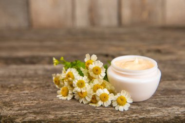 Tahta arka planda papatya esanslı vücut ve el kremi. Bitki dermatolojik kozmetik hijyen kremi. Doğal güzellik ürünü. Ahşap arka planda çiçekli kozmetik kremi. Spa konsepti. Boşluğu kopyala.