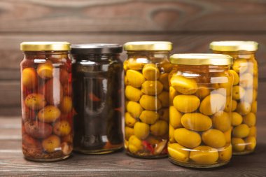 Kavanozda farklı türde zeytin. Cam kavanozda karıştırılmış zeytin turşusu. Ahşap bir arka planda. Ahşap masada lezzetli zeytinler. Yakın plan. Lezzetli sağlıklı Akdeniz yemekleri. Vejetaryen.