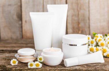 Kahverengi ahşap arka planda papatya çiçekli vücut ve el kremi. Bitki dermatolojik kozmetik hijyen kremi. Doğal kozmetik ürünü. Kozmetik tüpü. Ekolojik kozmetik. Uzayı kopyala.