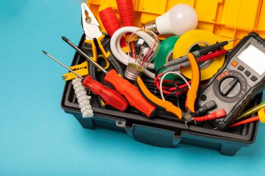 Mavi arka planda kopyalanmış elektrik teçhizatı. Üst görünüm. Elektrik aracı seti. Çoklu metre, test cihazı, tornavida, kesici, koli bandı, lamba, mezura, mezura ve kablo..